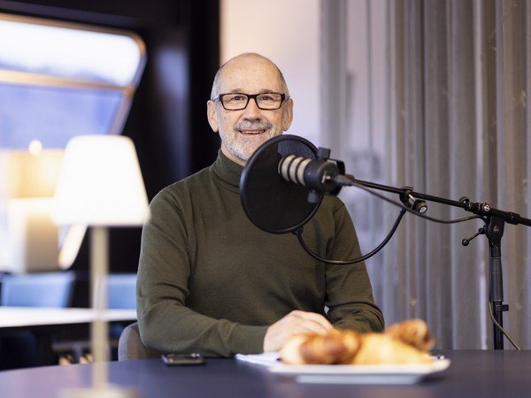 René Hutter hinter dem Podcast-Mikrophon am Tisch sitzend