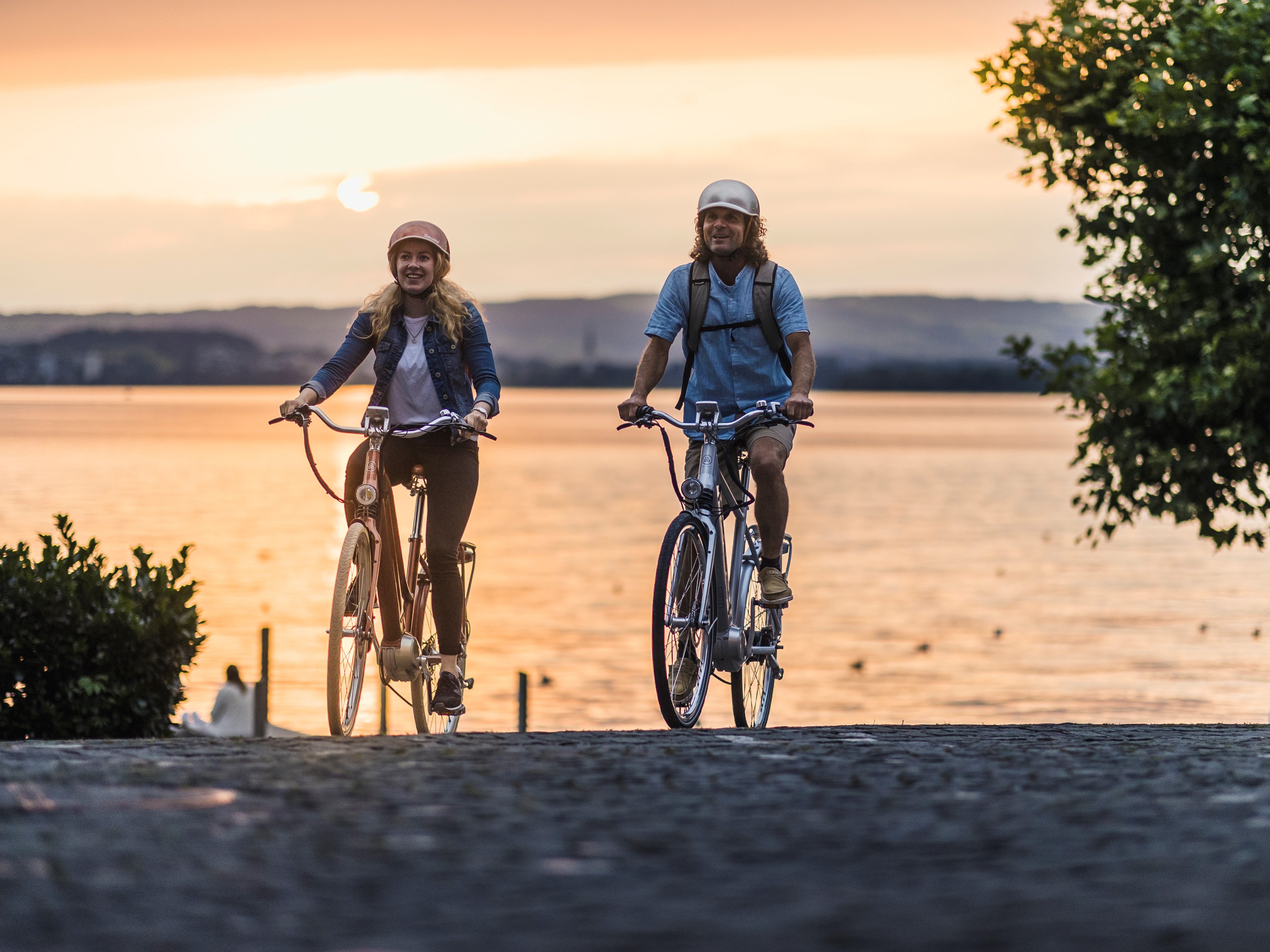 Zwei Velofahrer mit See im Hintergrund in Abendstimmung