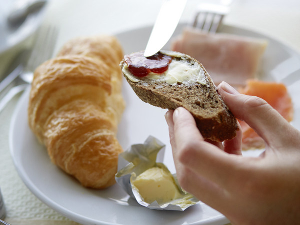 Frühstücksteller mit Gipfeli & Butter, Hände halten ein mit Konfitüre bestrichenes Brot