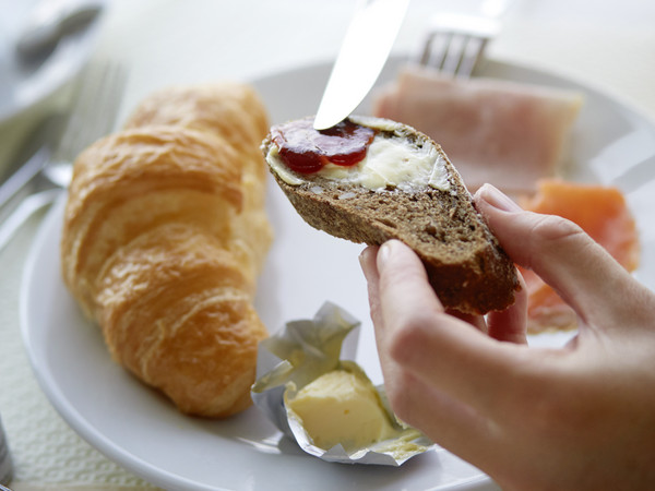 Frühstücksteller mit Gipfeli & Butter, Hände halten ein mit Konfitüre bestrichenes Brot