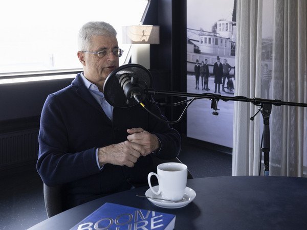 Gianni Bomio am Podcast Tisch hinter dem Mirkophon mit seinem Buch auf dem Tisch