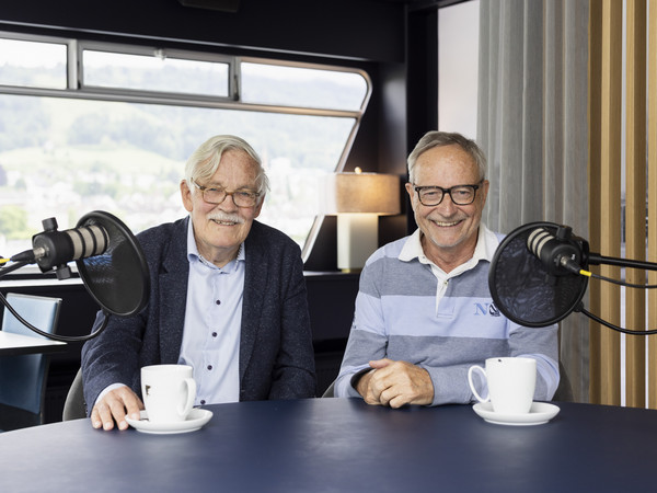 Jürg Meister und Heinz Amstad im Porträt am Podcast-Tisch sitzend vor den Mikrophonen