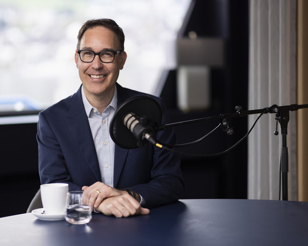 Remo Rey vor dem Podcast Mikrophon mit Kaffeetasse