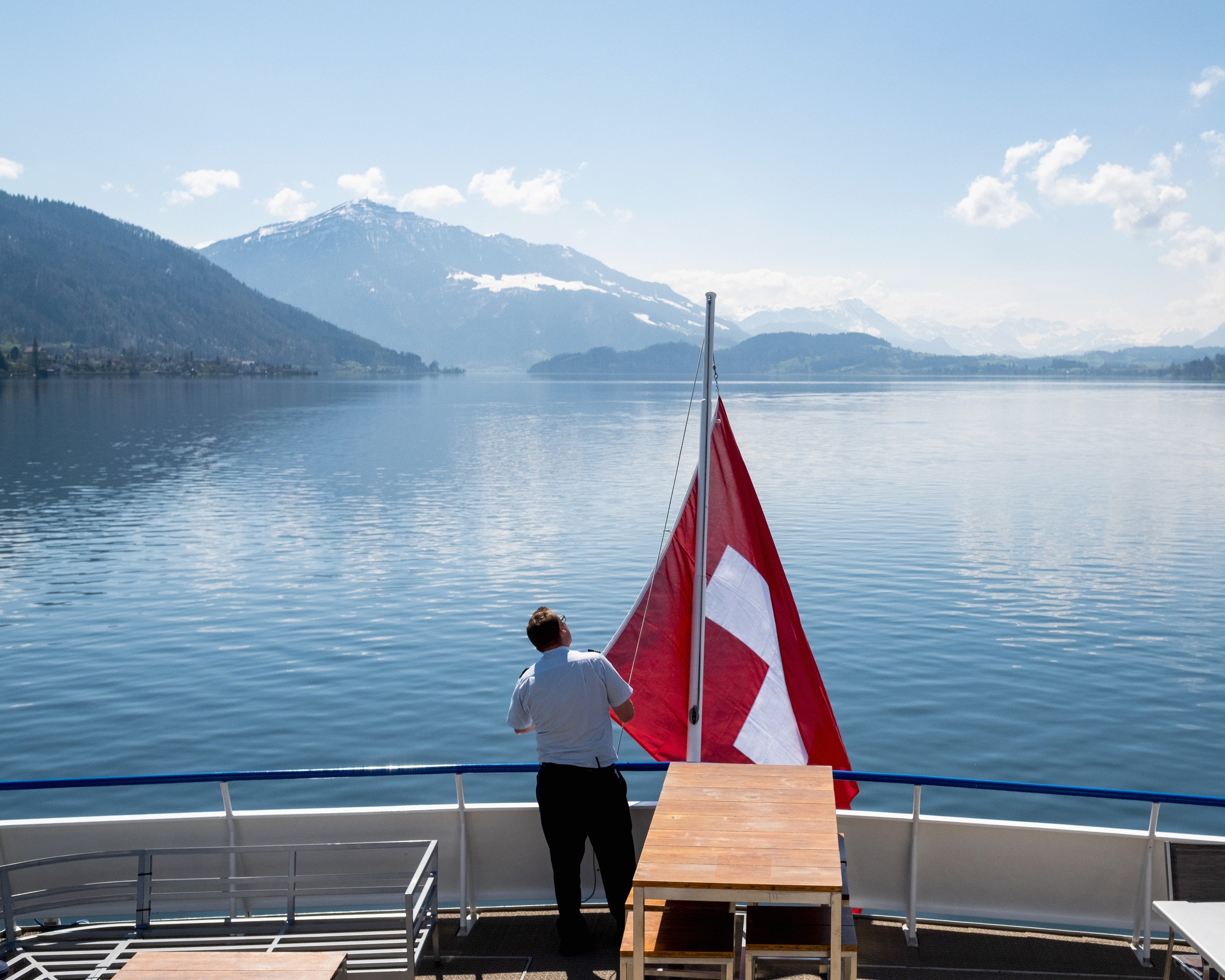 Sailor hoisting the Swiss flag on the stern with a view of the lake