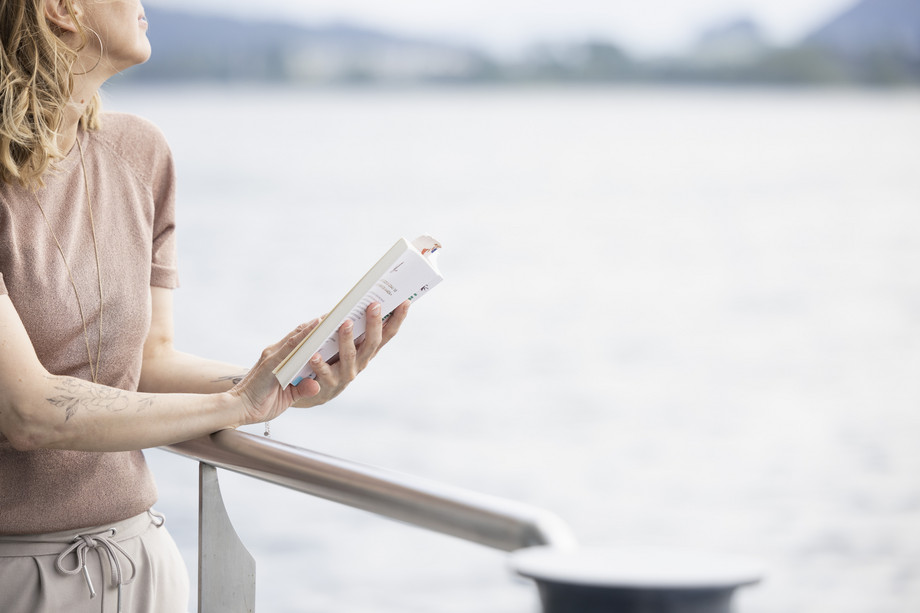 Hygge Zeit auf dem Schiff Frau lesend an der Reling mit Blick auf den See